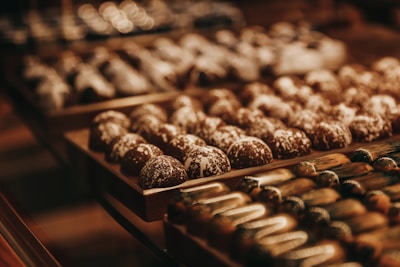 A variety of artisanal chocolates are displayed on wooden trays. The chocolates appear in different shapes and are decorated with intricate designs, featuring a glossy and smooth finish.