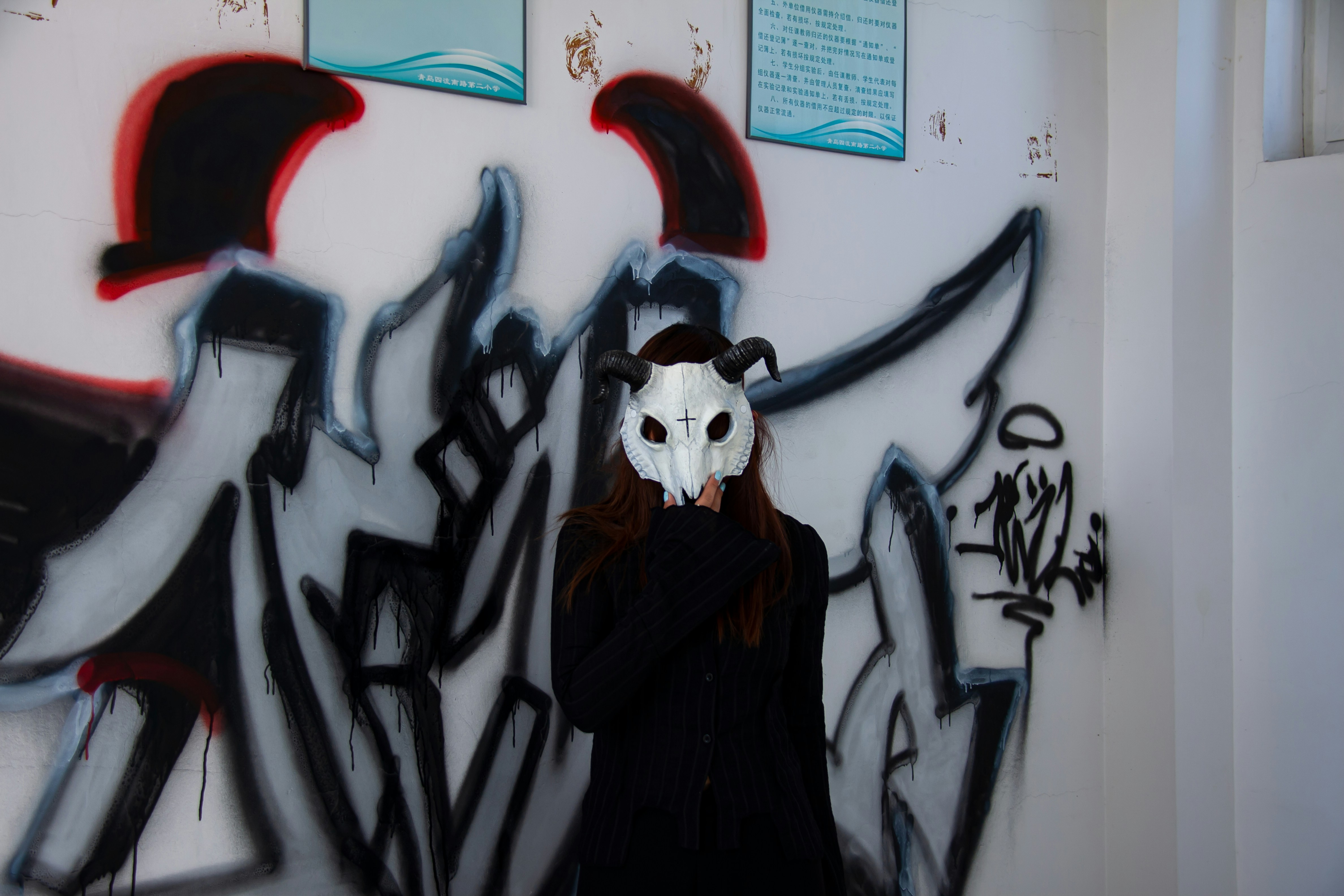 A woman wearing a mask standing in front of a wall covered in graffiti ...