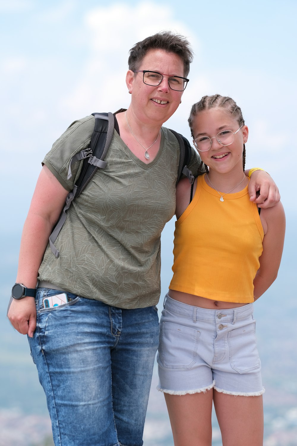 a woman standing next to a young girl on top of a mountain