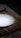 A white ceramic plate is placed on a woven bamboo placemat, which rests on a floral patterned tablecloth. The lighting creates a soft shadow around the plate, enhancing the contrast between the smooth white surface and the dark placemat.