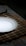 A white ceramic plate is placed on a woven bamboo placemat, which rests on a floral patterned tablecloth. The lighting creates a soft shadow around the plate, enhancing the contrast between the smooth white surface and the dark placemat.