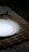 A white ceramic plate is placed on a woven bamboo placemat, which rests on a floral patterned tablecloth. The lighting creates a soft shadow around the plate, enhancing the contrast between the smooth white surface and the dark placemat.