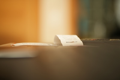 A close-up of a small paper receipt partially protruding from a machine, likely a cash register or printer. The background is softly blurred, creating a warm ambiance.