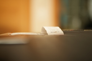A close-up of a small paper receipt partially protruding from a machine, likely a cash register or printer. The background is softly blurred, creating a warm ambiance.