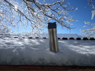 A vibrant Frostara thermos nestled in a snowy mountain backpack.