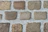 A close-up view of a cobblestone pavement with rectangular stones arranged in a regular pattern. The stones vary in shades of brown and gray, and the gaps between the stones are filled with cement.