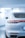 A sleek, white luxury car is parked in a brightly lit showroom. The focus is on the rear of the car, showcasing its modern design, including the streamlined taillights and dual exhaust pipes. The environment is pristine and well-lit, emphasizing the car's polished exterior.