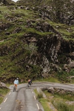 Cyclists riding along a scenic path surrounded by green hills and traditional village views.