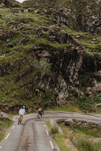Cyclists riding along a scenic path surrounded by green hills and traditional village views.