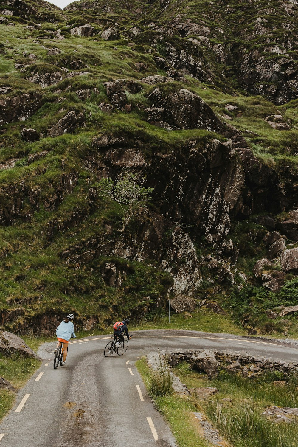 a man riding a bike down a road next to a lush green hillside