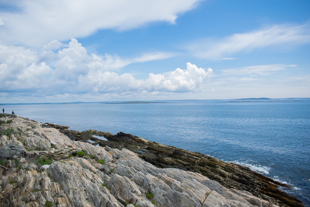 a couple of people standing on top of a rocky cliff next to the ocean