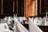 A luxurious dining setup featuring elegantly folded white napkins, sparkling glassware, and floral centerpieces arranged on round tables. The room is adorned with wooden paneling and framed portraits, creating an opulent and classic atmosphere.