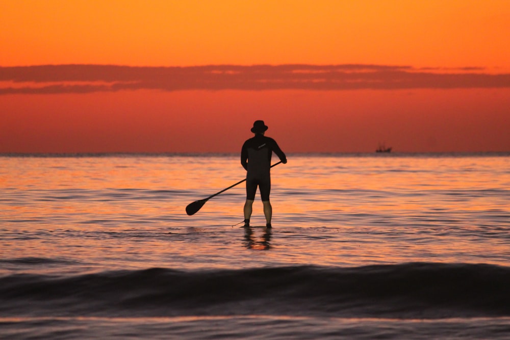 a man standing on a surfboard in the ocean at sunset