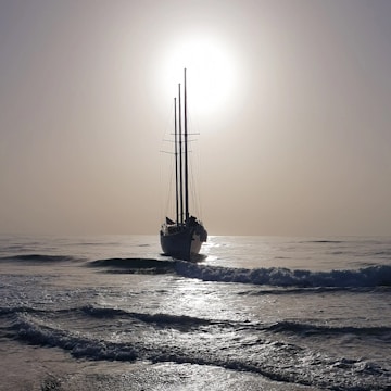 A sunlit sailboat cutting through gentle waves at dawn.