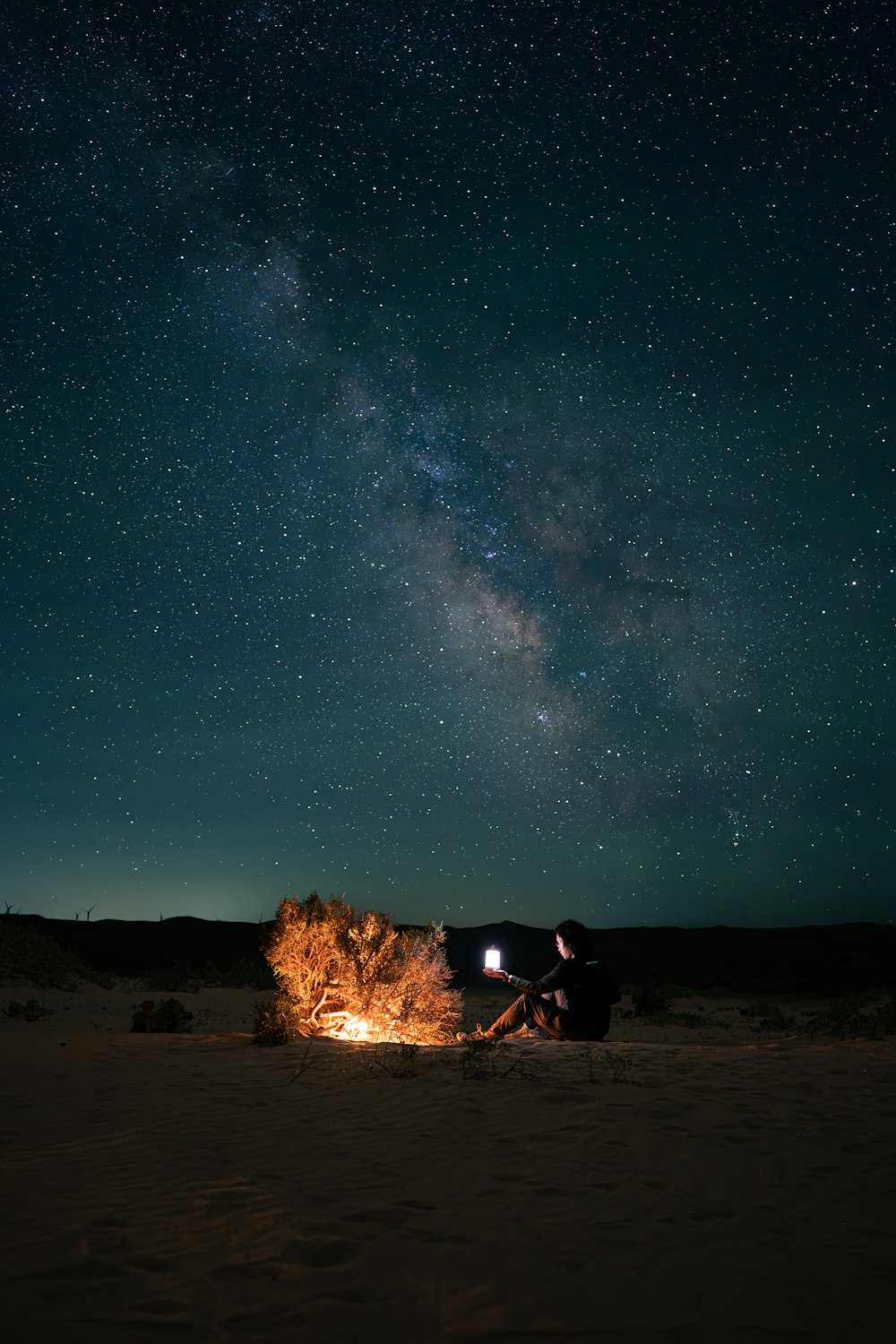 a man sitting next to a campfire under a night sky filled with stars