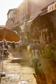 A sunlit street corner in a bustling foreign city, with colorful market stalls and locals going about their day.