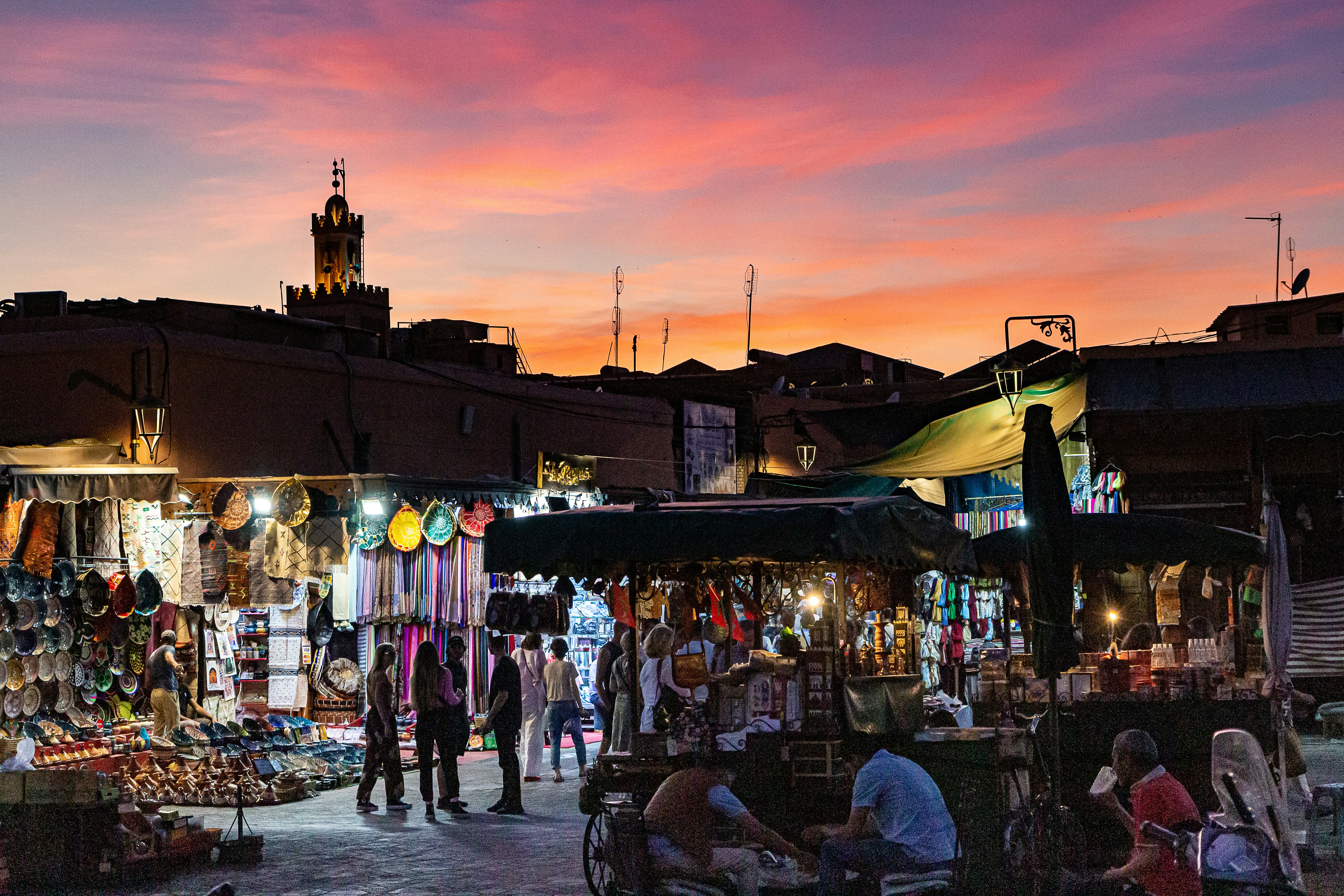 Plaza Jemaa el-Fna al atardecer con puestos de comida iluminados, minarete de Koutoubia al fondo, cielo violeta y naranja