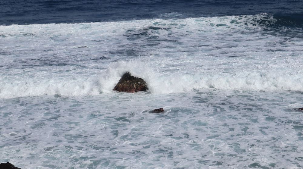 a rock sticking out of the ocean next to a wave