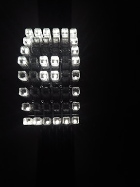 A geometric arrangement of multiple small, rectangular light cubes emitting a bright, white light against a dark background. The cubes are organized in a grid-like, three-dimensional structure, creating a striking visual effect.