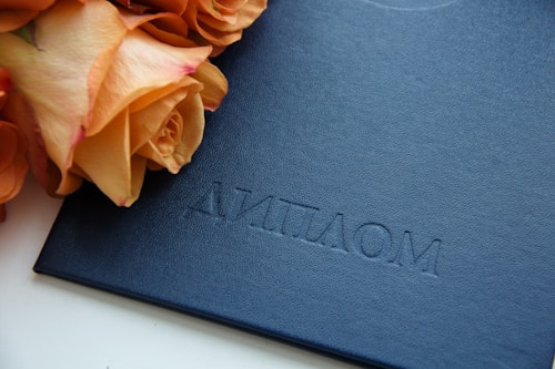 A dark blue textured document folder embossed with the word 'ДИПЛОМ' lies next to a bouquet of peach-colored roses.