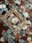 A collection of various coins is scattered across the surface, with a vintage, ornate golden frame placed centrally around one of the coins. The coins vary in color and denomination, with some depicting designs and figures.