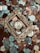 A collection of various coins is scattered across the surface, with a vintage, ornate golden frame placed centrally around one of the coins. The coins vary in color and denomination, with some depicting designs and figures.
