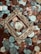A collection of various coins is scattered across the surface, with a vintage, ornate golden frame placed centrally around one of the coins. The coins vary in color and denomination, with some depicting designs and figures.