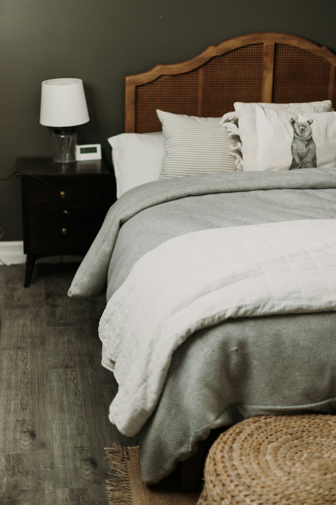 Dark wood nightstand beside a bed with cream linen bedding and a lamp