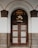 An ornate wooden door with glass panels featuring a decorative grid pattern stands beneath a large arched entryway. The arch is framed by light gray and dark brown stonework, adding a feeling of elegance. The door is set in a white wall and there are intricate glass panes above the door.
