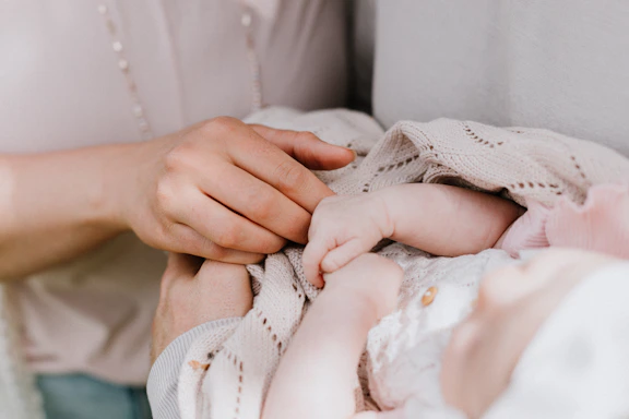 A pair of tiny baby hands gently wrapped in a soft knitted blanket, resting peacefully.