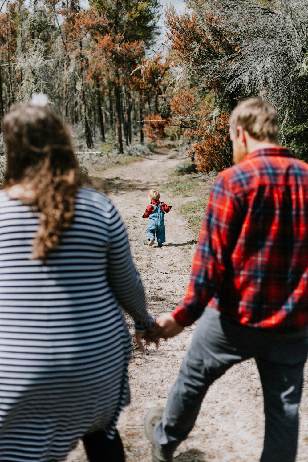 a man and a woman holding hands while walking down a dirt road