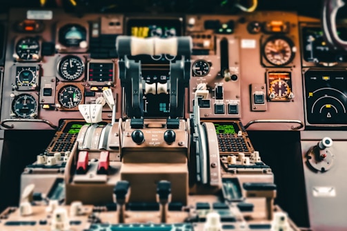 A detailed and busy cockpit of an aircraft with numerous dials, gauges, and switches. The central focus is on the throttle levers and control panels with various indicators and meters. The dashboard is designed for navigation and monitoring flight operations, encompassing a range of technical instruments.