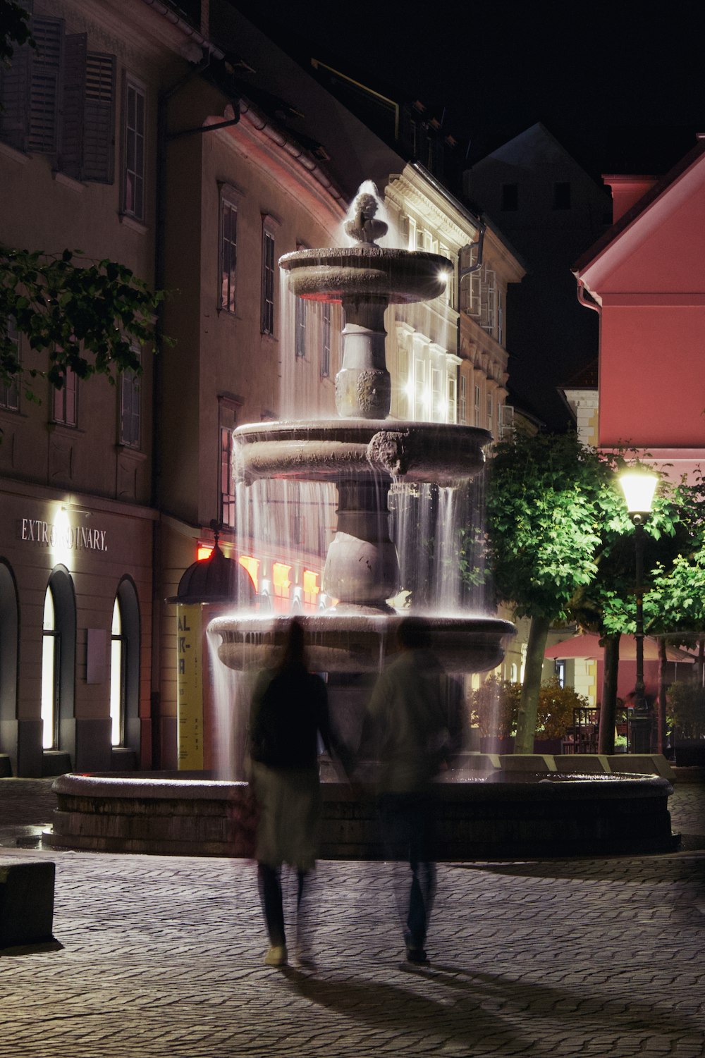 two people standing in front of a fountain at night