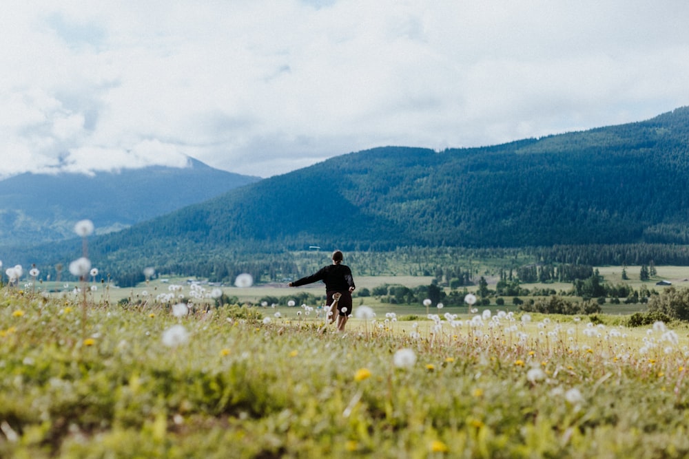 a man is walking through a field with mountains in the background