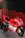 A red and white Ducati racing motorcycle is displayed on a metallic platform. It is adorned with various sponsor logos, including TIM, Shell, and Bridgestone, and features the number 04. The background consists of diagonal red and black patterned panels.