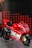 A red and white Ducati racing motorcycle is displayed on a metallic platform. It is adorned with various sponsor logos, including TIM, Shell, and Bridgestone, and features the number 04. The background consists of diagonal red and black patterned panels.