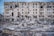 A severely damaged multi-story building with multiple broken windows and structural damage. Surrounding the building are piles of rubble and debris, including broken concrete and exposed metal. The scene indicates a recent event of destruction.