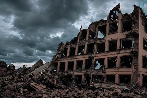 A partially collapsed multi-story building with exposed interiors and broken concrete, surrounded by rubble. The sky is overcast with dark, dramatic clouds adding a sense of tension and foreboding.