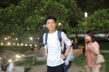 A photo of a young student smiling with a backpack in front of a famous university campus.