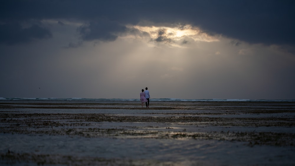 a couple of people standing on top of a beach under a cloudy sky