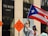 A woman wearing a red top and blue hat is waving a Puerto Rican flag in front of a Ted Baker London store. Two road work signs, reading 'ROAD WORK 500 FT', are visible nearby, suggesting construction in the area.