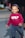 A young child is happily walking on a paved surface. The child is wearing a red sweatshirt with the words 'ONLY FOR YOU' printed on it and patterned pants. A hat with a blue and white anchor pattern adorns their head. In the background, an adult's leg is partially visible, and there is a blurred view of cars and a street.