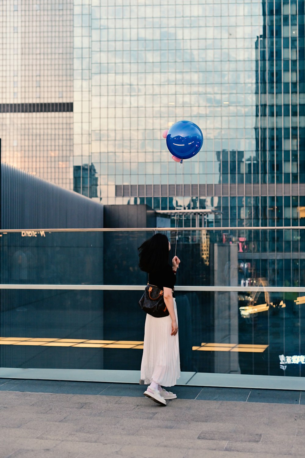 a woman in a white dress is flying a blue balloon