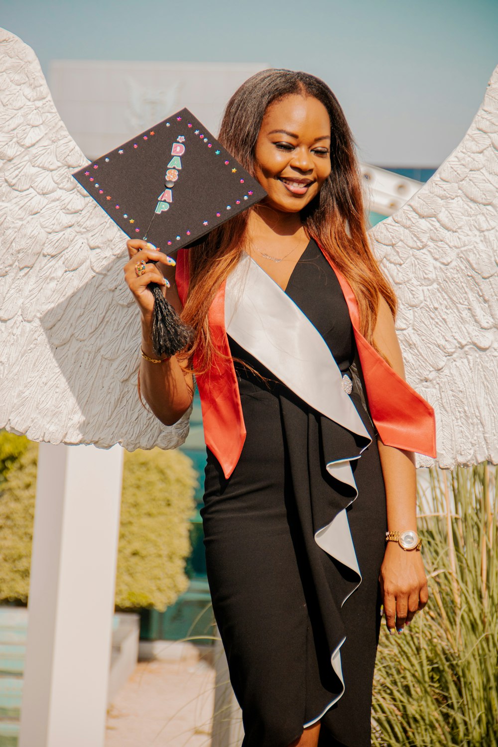 a woman in a black dress holding a black and white graduation cap