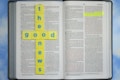 An open Bible with highlighted text in the book of John. Yellow tiles with blue letters are arranged in the shape of a cross spelling 'the good news.' The background is a soft blue sky pattern.