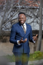A confident, well-dressed male escort smiling warmly in an urban setting at dusk.