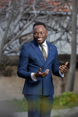 A confident, well-dressed male escort smiling warmly in an urban setting at dusk.