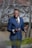 A well-dressed man in traditional attire standing confidently in an elegant outdoor setting.
