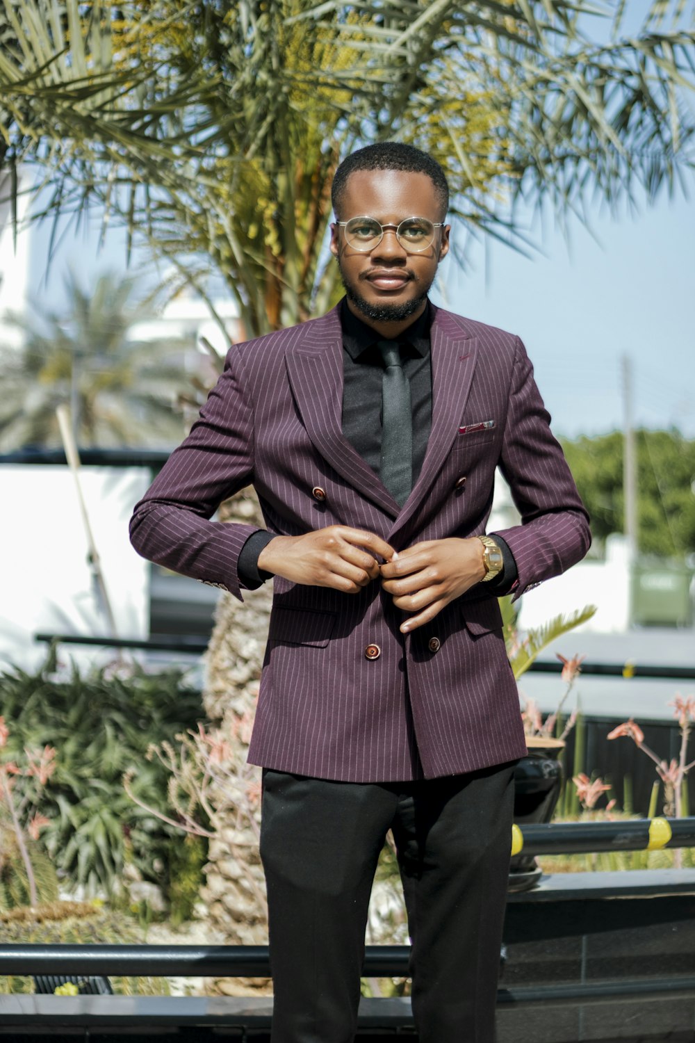 a man in a suit standing in front of a palm tree