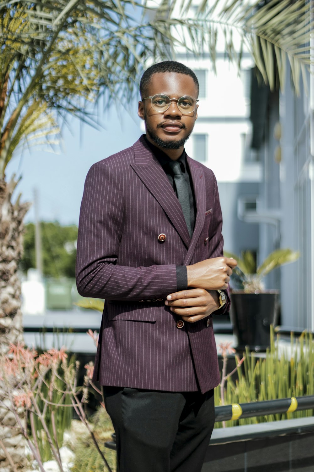 a man in a suit standing in front of a palm tree